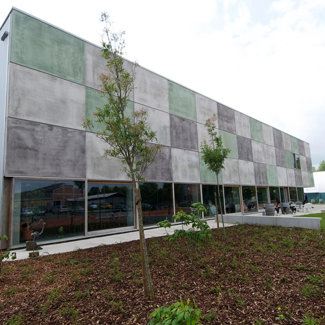 DCA Sportcomplex - buitenkant. De onderste verdieping bevat grote ramen. Het gebouw is opgebouwd met een combinatie van materialen. De buitenkant van het gebouw bestaat uit lichtgrijze, donkergrijze en groene rechthoeken.