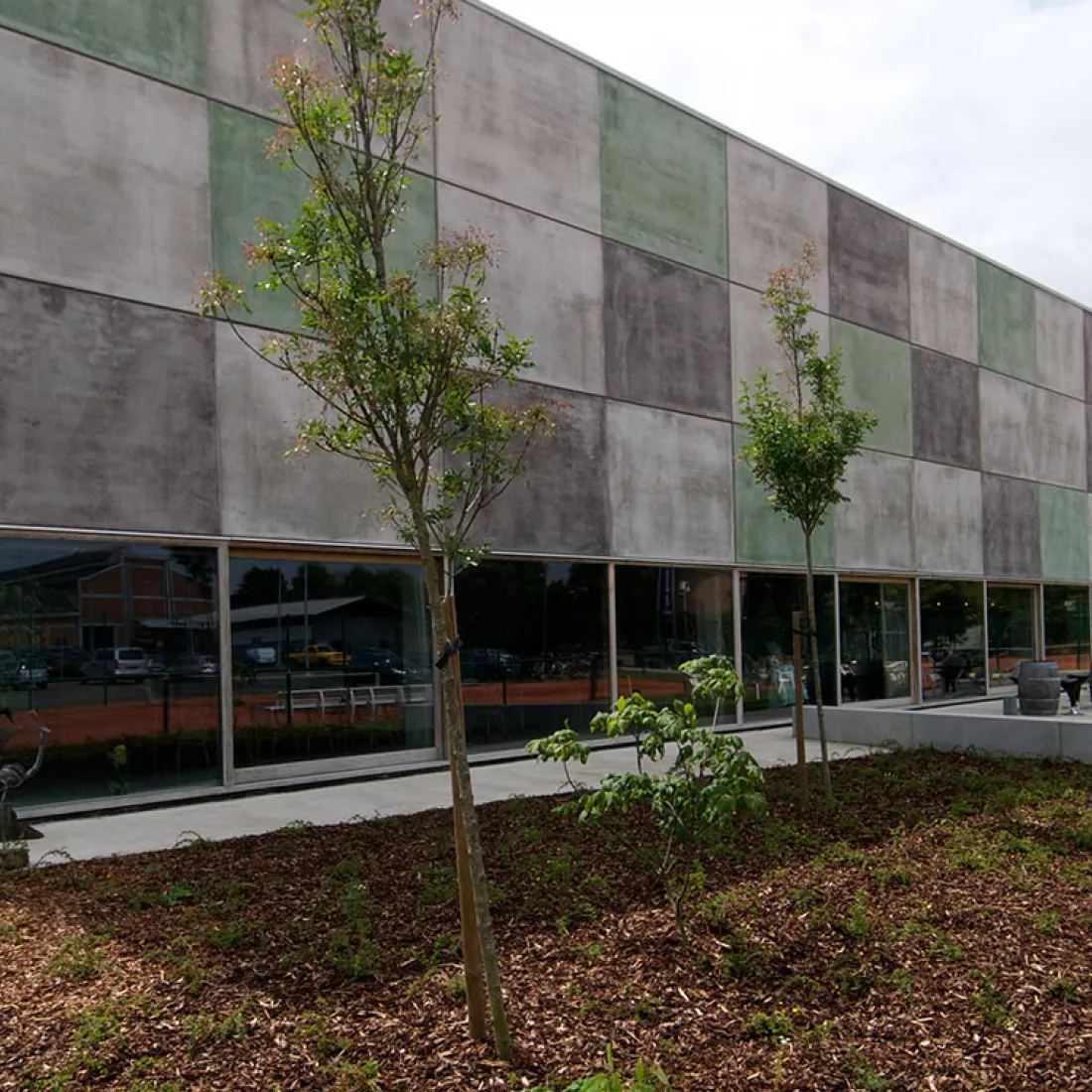 DCA Sportcomplex - buitenkant. De buitenkant van het gebouw bestaat uit donkergrijze, lichtgrijze en groene rechthoeken. De onderste verdieping bestaat uit grote ramen.