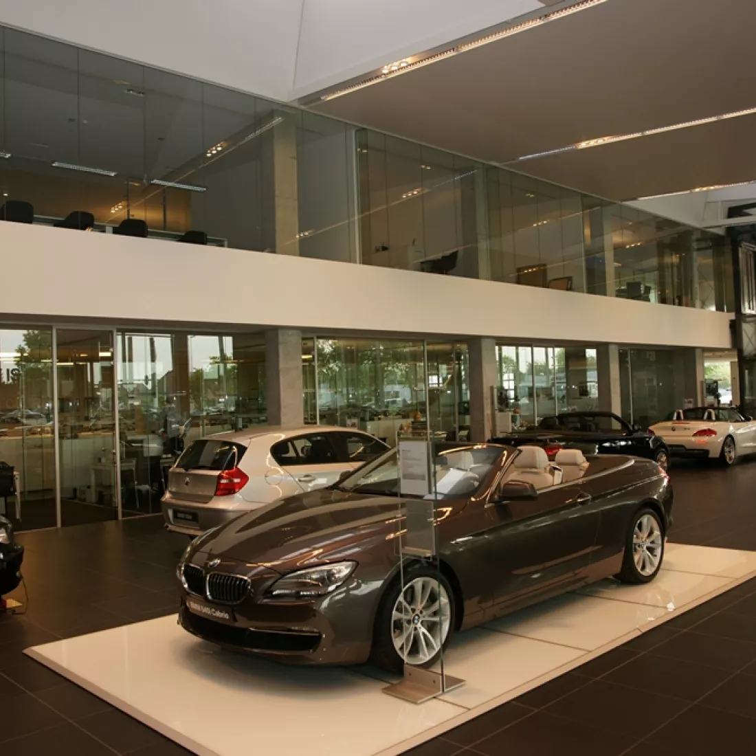 Binnenkant Centrauto - showroom. Het gebouw bestaat uit twee verdiepingen. Op de beneden verdieping staan er verschillende auto's tentoongesteld. Achter de auto's bevindt zich een glazenwand. Op de bovenste verdieping bevinden zich kantoren.