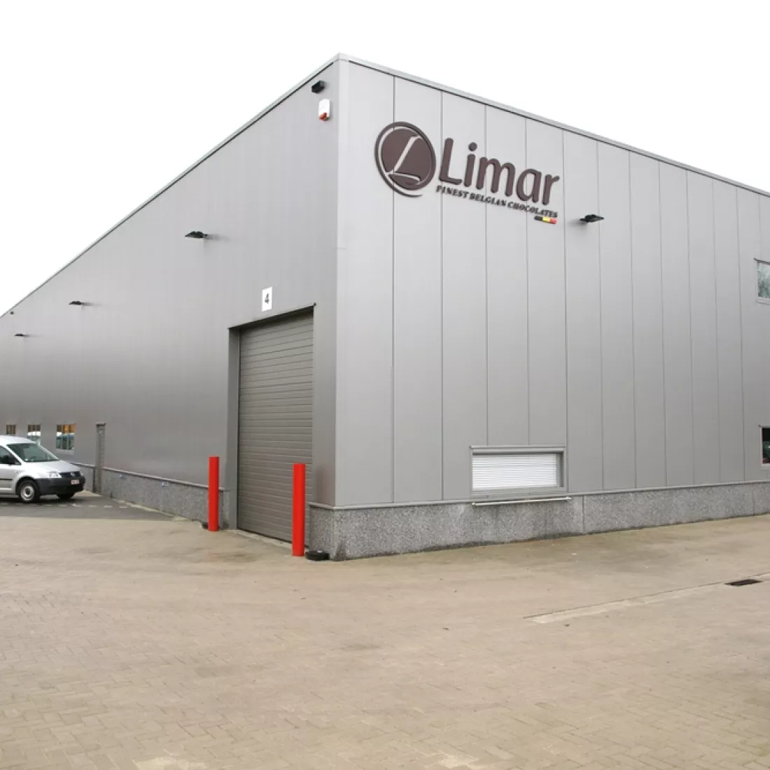 Zijaanzicht productieruimte Limar. Het gebouw is grijs en heeft ook een grijze poort. Het logo van Limar is aan de muur te vinden. Het gebouw is gemaakt van staal.