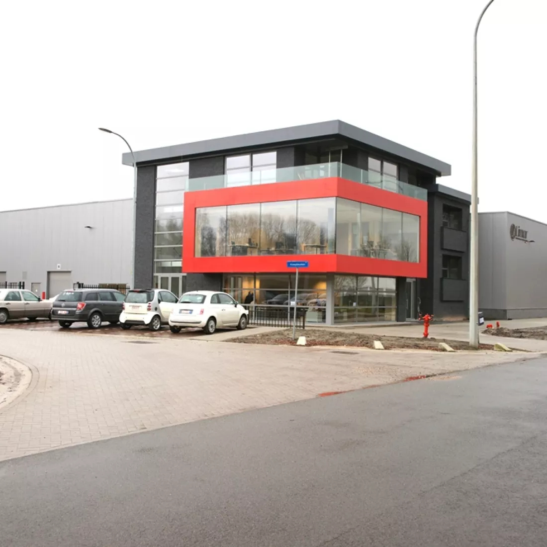 Zijaanzicht kantoor en productieruimte met magazijn van Limar. Het gebouw is gemaakt uit staal. Het bevat de kleuren grijs, zwart en rood. Het kantoor heeft veel ramen en bevat drie verdiepingen.