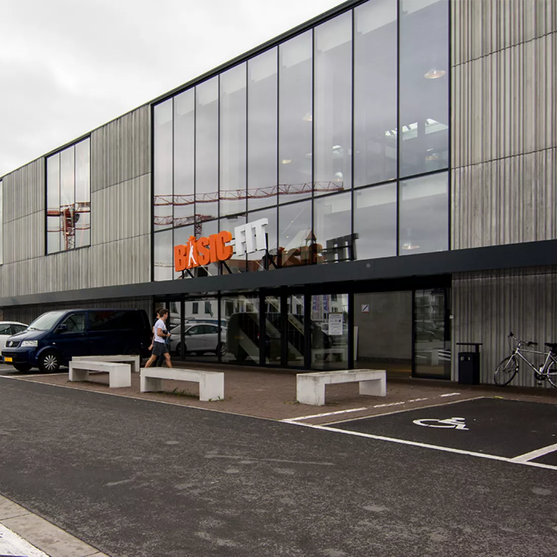 Vooraanzicht Basic Fit. Vooraanzicht Basic Fit. Het gebouw heeft veel ramen en is opgebouwd met beton.