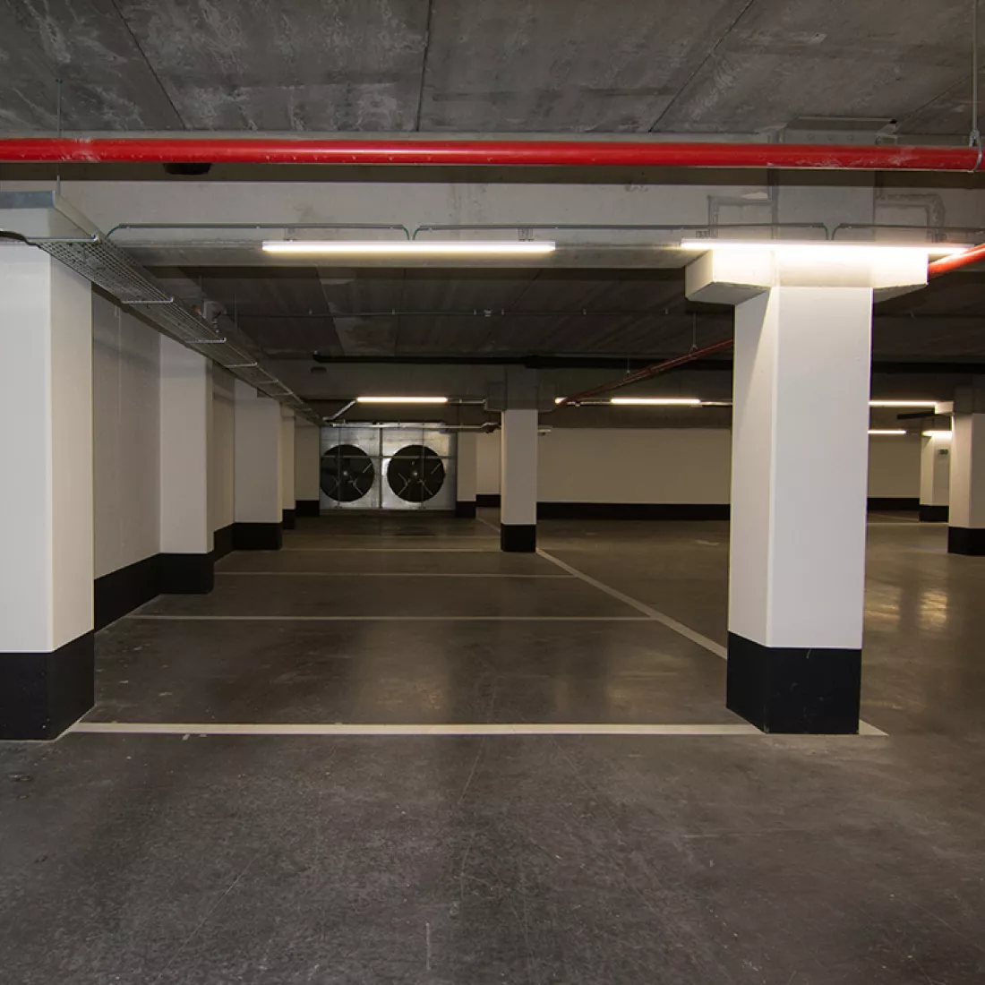 Binnenkant parking Duin & Water shops. Binnenkant parking Duin & Water shops. De parking is gebouwd met beton. Er staan betonnen pilaren die wit geschilderd zijn. Aan de onderkant zijn de pilaren zwart. De vloer is zwart en met witte lijnen zijn de parkeerplaatsen afgebakend De muren van de parking zijn ook wit geschilderd.