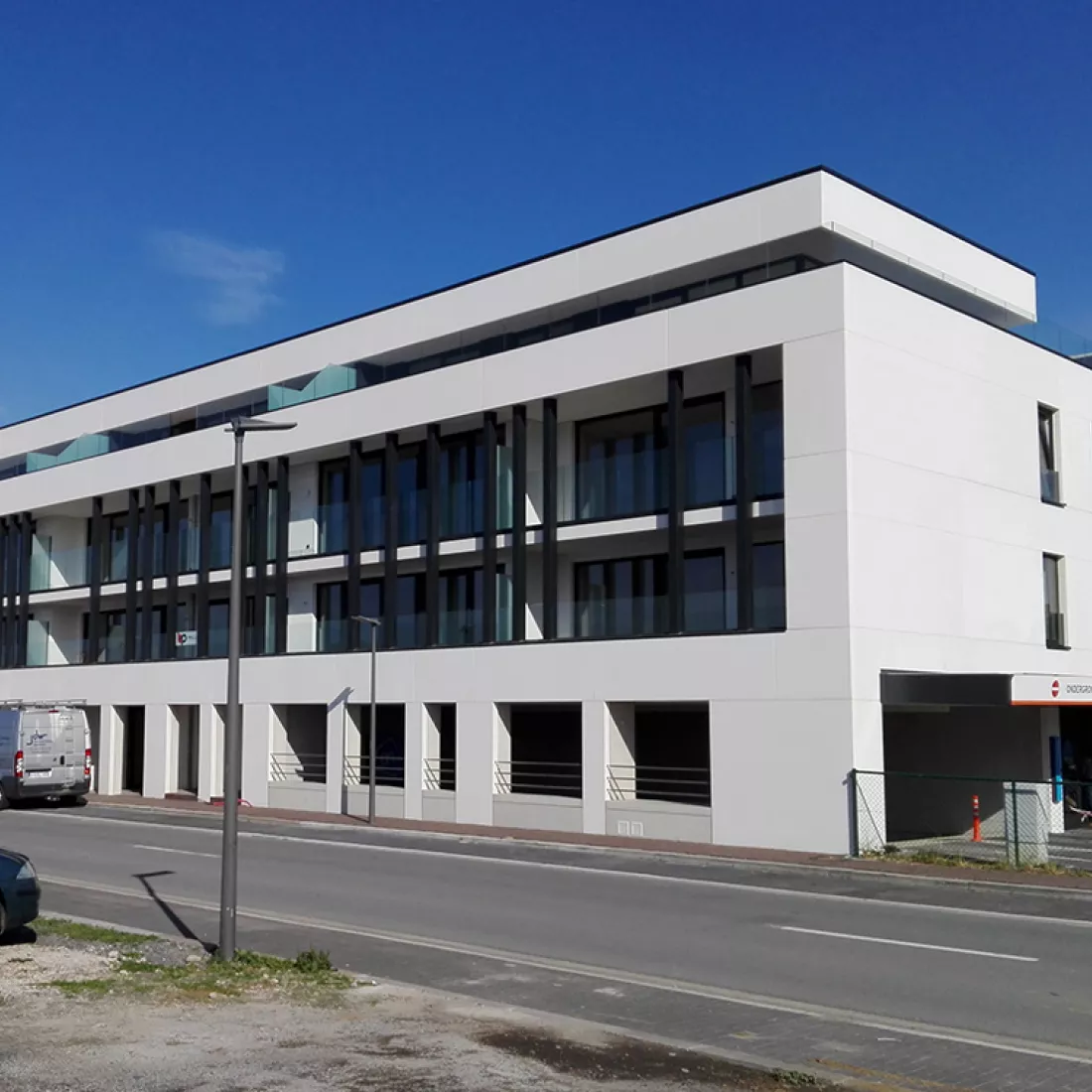 Duin & Water shops. Duin & Water shops. Het gebouw is gebouwd met beton. Het bestaat uit witte platen. Het heeft vier verdiepingen. De bovenste drie verdiepingen hebben een balkon. Bij elk balkon bevinden zich zwarte balken. De gelijkvloers is een parking.