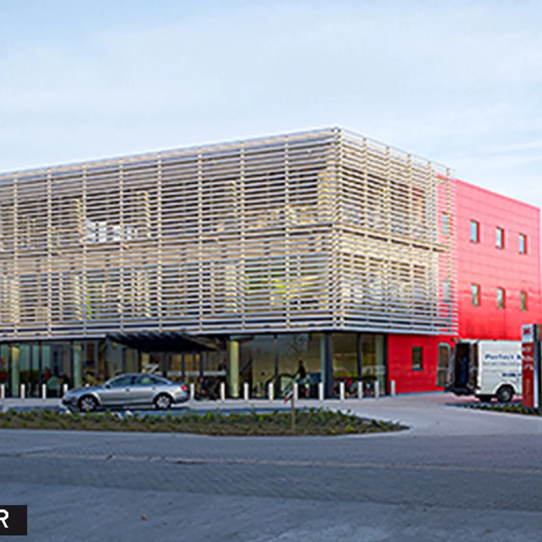 Werkgebouw DIBO voor renovatie gevel. Het gebouw bevat grote ramen aan de voorkant. Langs de zijkant bevat het gebouw rode tegels en kleinere ramen.