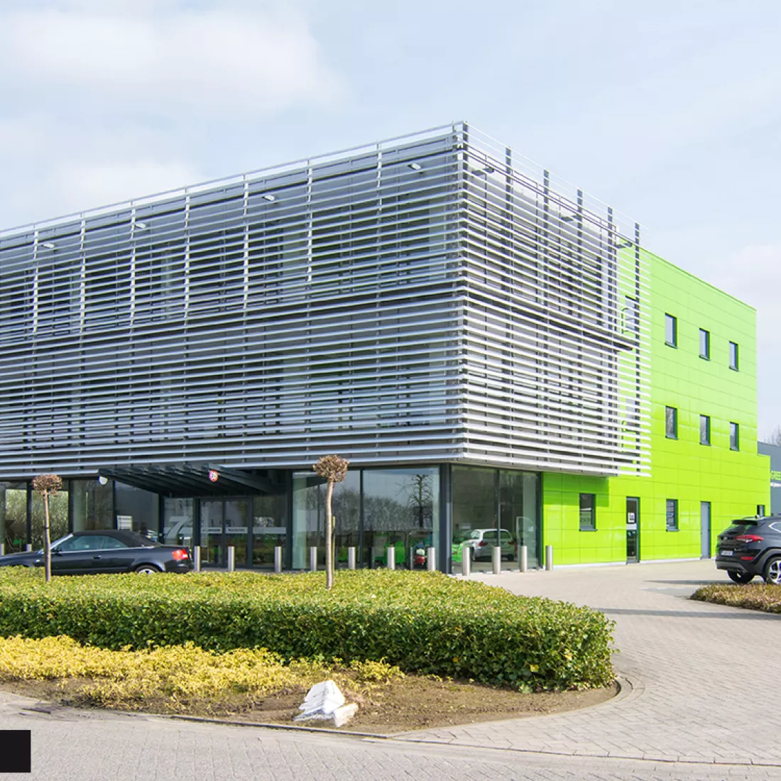 Werkgebouw DIBO na renovatie gevel. Het gebouw bevat grote ramen aan de voorkant. Langs de zijkant bevat het gebouw groene tegels en kleinere ramen.