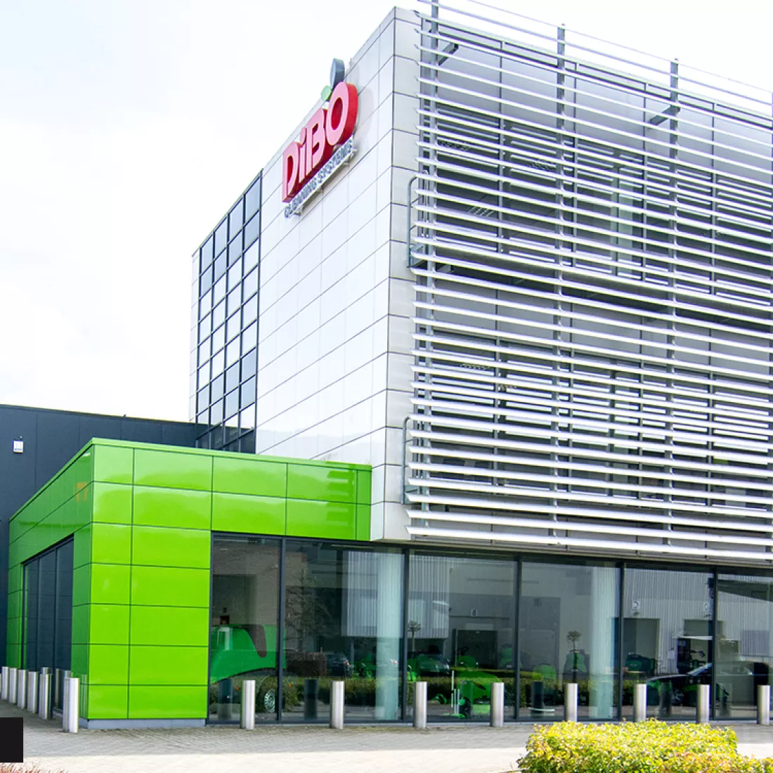 Zijaanzicht werkgebouw DIBO na renovatie gevel. De eerste verdieping bevat groene tegels. Bovenaan het gebouw hangt het logo van DIBO.