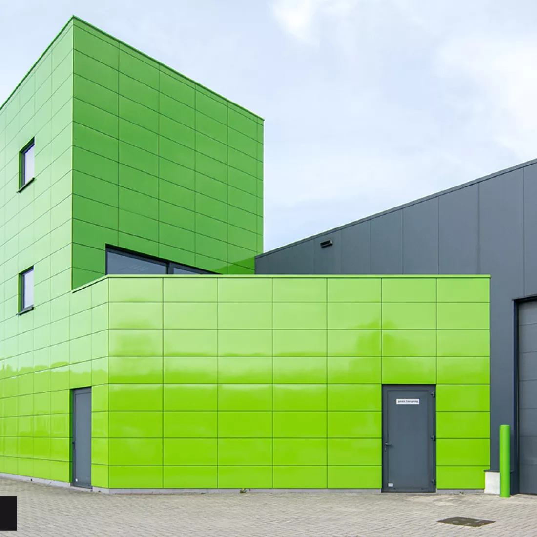 Zijaanzicht werkgebouw DIBO na renovatie gevel. Het gebouw bevat groene tegels en ramen met zwarte omranding. De deuren zijn ook zwart.