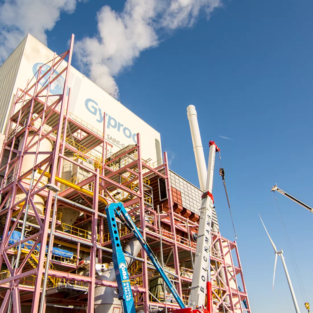 Opbouw MCC-gebouw Gyproc. Voor het gebouw staan rode met gele stellingen en werkmaterialen.