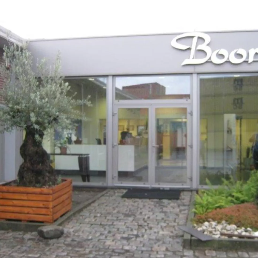 Vooraanzicht Boortmalt inkom. Het gebouw is grijs en opgebouwd met staal. De inkom bevat een glazendeur. Naast de deur bevinden zich grote ramen.