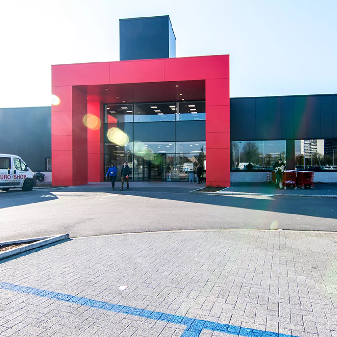 Inkom handelsruimten Immo Euro. Tegen het gebouw hangen zwarte platen en de inkom bestaat uit rode platen.