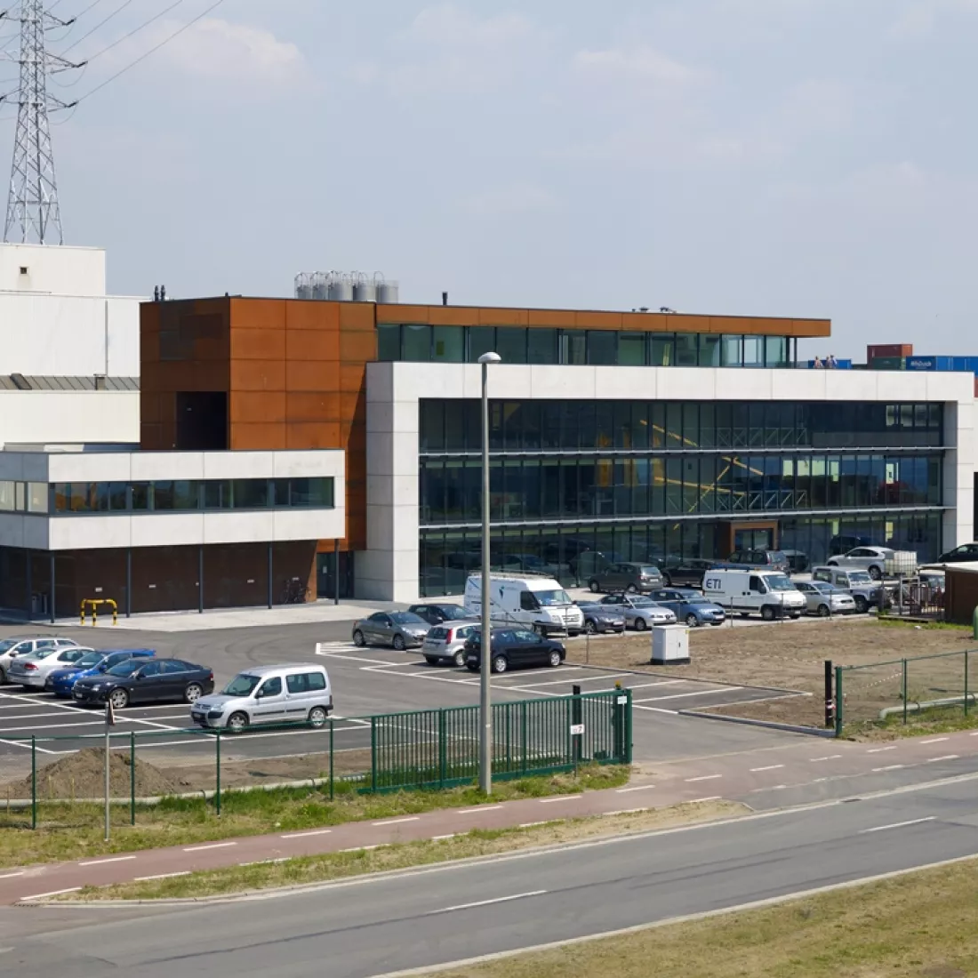 Bovenaanzicht Ivens kantoor. Rond het gebouw bevindt zich een groene poort en hek. Het gebouw bestaat uit vier verdiepingen. De eerste drie verdiepingen rechts bestaan uit witte platen en heel veel ramen. Het vierde verdiep bestaat uit een bruine, roestachtige plaat. De eerste verdieping links bestaat ook uit deze kleur plaat. Het tweede verdiep rechts bestaat uit een witte plaat.