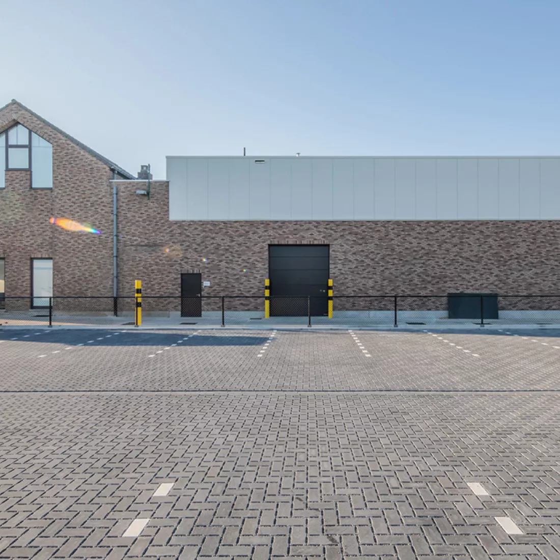 Vooraanzicht nieuwbouw Nauta Holding. Tijdens de opbouw is er staal gebruikt. Het magazijn bestaat uit rode steen en grijze wanden. Het bevat een zwarte poort en deur.