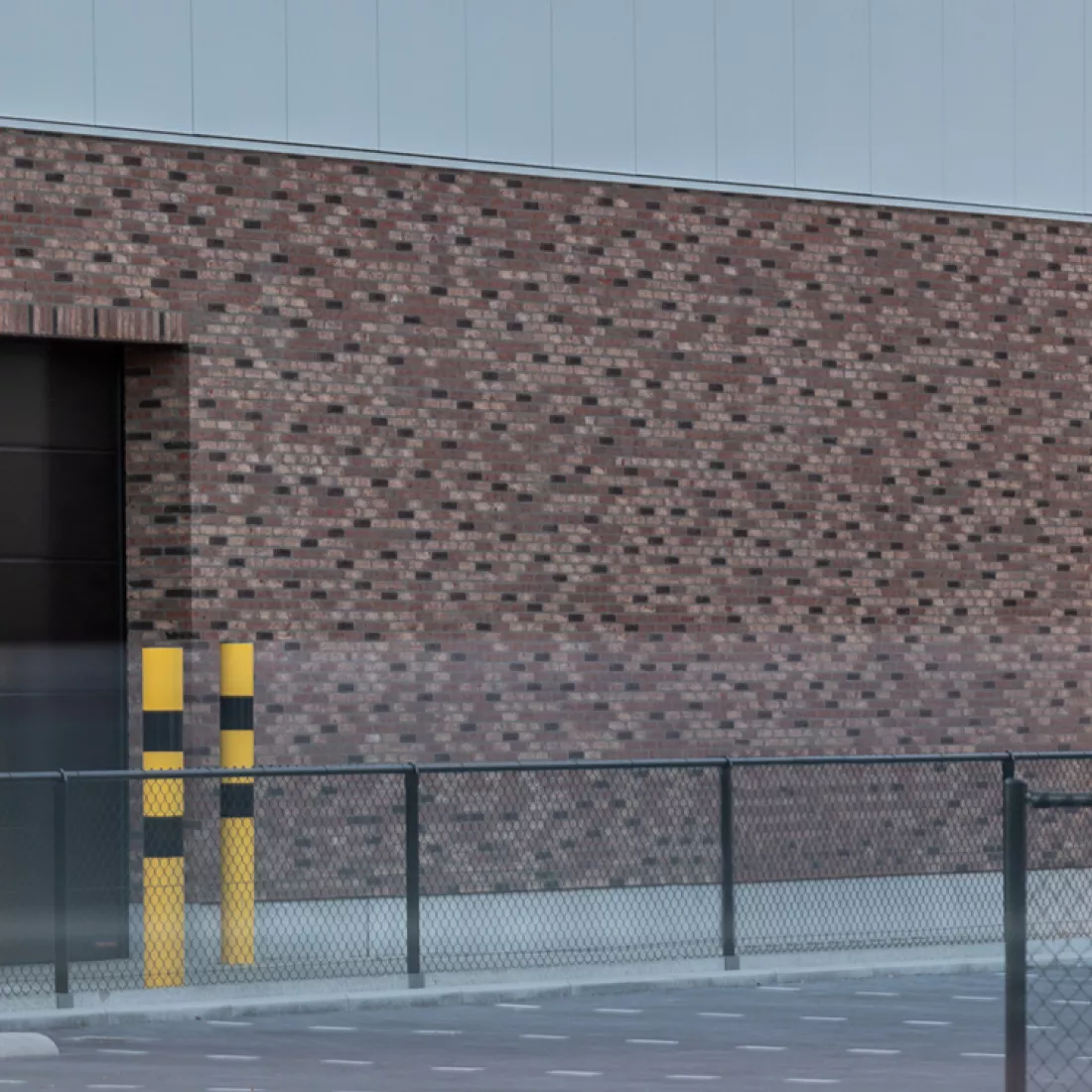 Close-up muur nieuwbouw magazijn Nauta Holding. De muur bestaat beneden uit rode steen en aan de bovenkant uit grijze wanden. Links bevindt zich een zwarte poort.