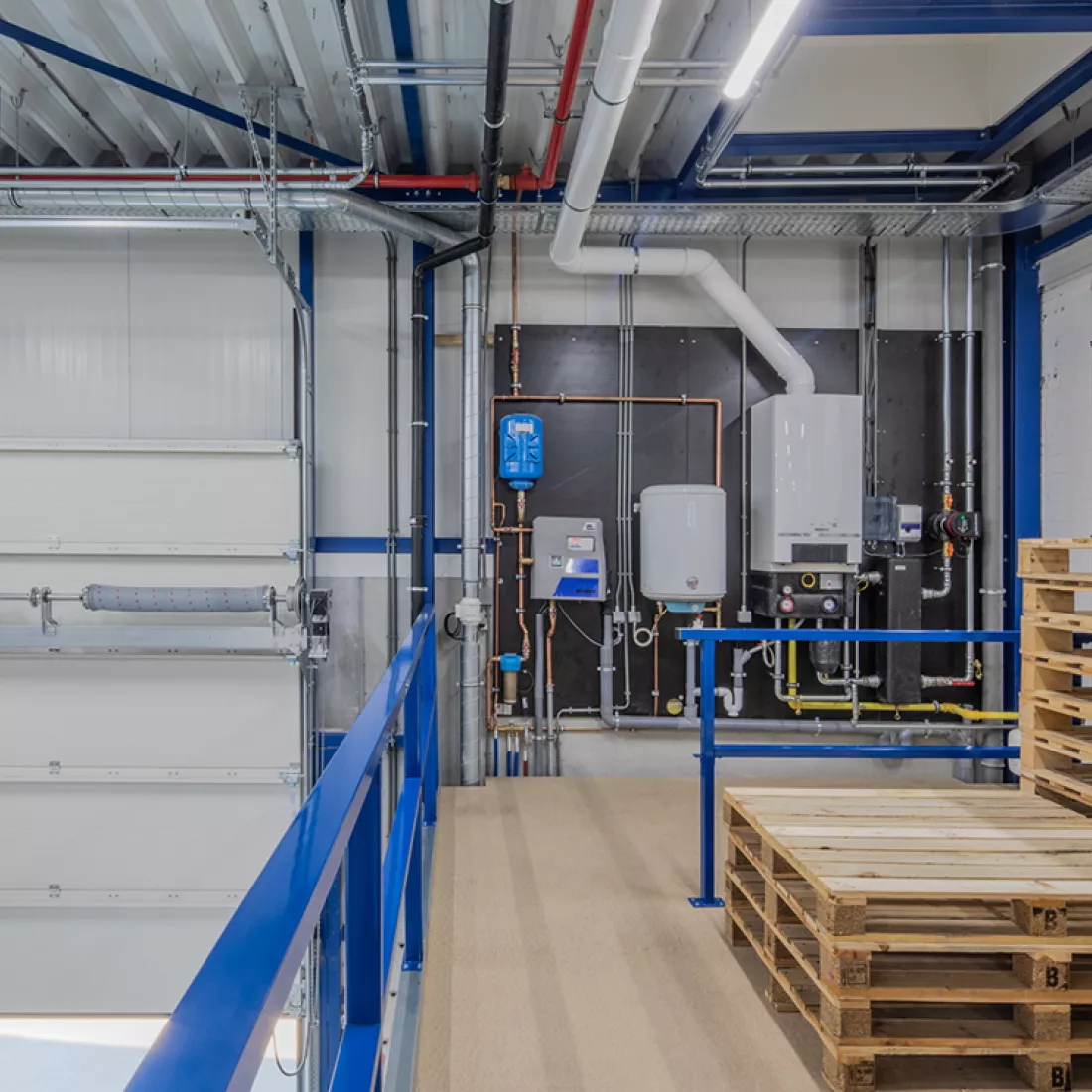 Binnenkant nieuwbouw magazijn Nauta Holding. Links bevindt zich de poort. De afbeelding is gemaakt vanaf de tweede verdieping. De railing van deze verdieping is blauw. Er liggen rechts paletten opgestapeld. Achteraan bevindt zich apparatuur zoals een boiler. 
