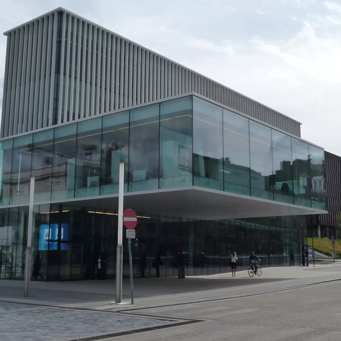 Zijaanzicht kantoor KBC Leuven. Het kantoor bestaat uit grote ramen. Een deel van de tweede verdieping steekt iets meer naar voren. Bovenaan heeft het gebouw witte balken voor de ramen.