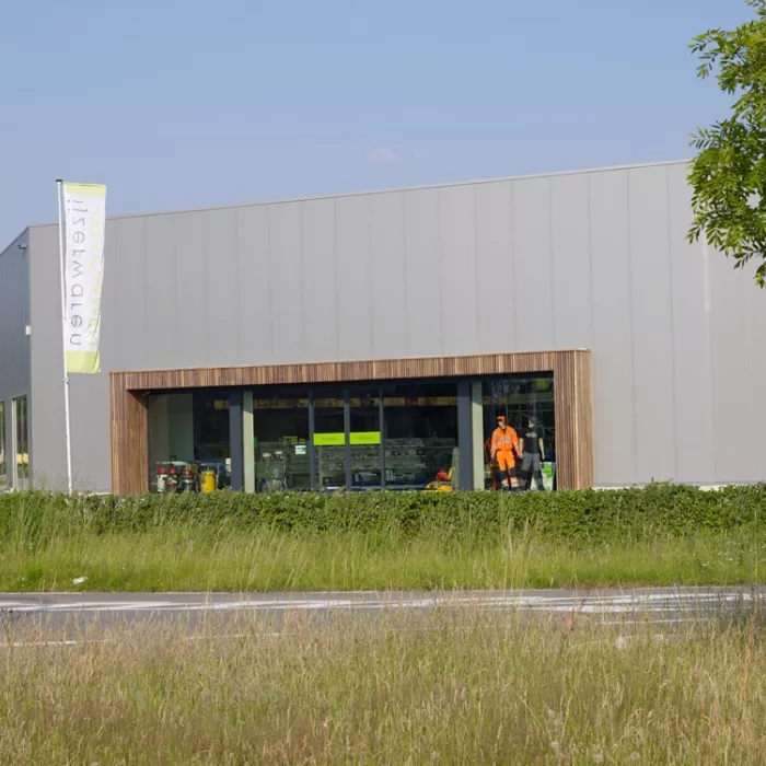 Vooraanzicht winkel Vertommen ijzerwaren. De afbeelding is genomen vanaf de overkant van de straat. De omranding van de winkelramen bestaat uit een houtenlook.