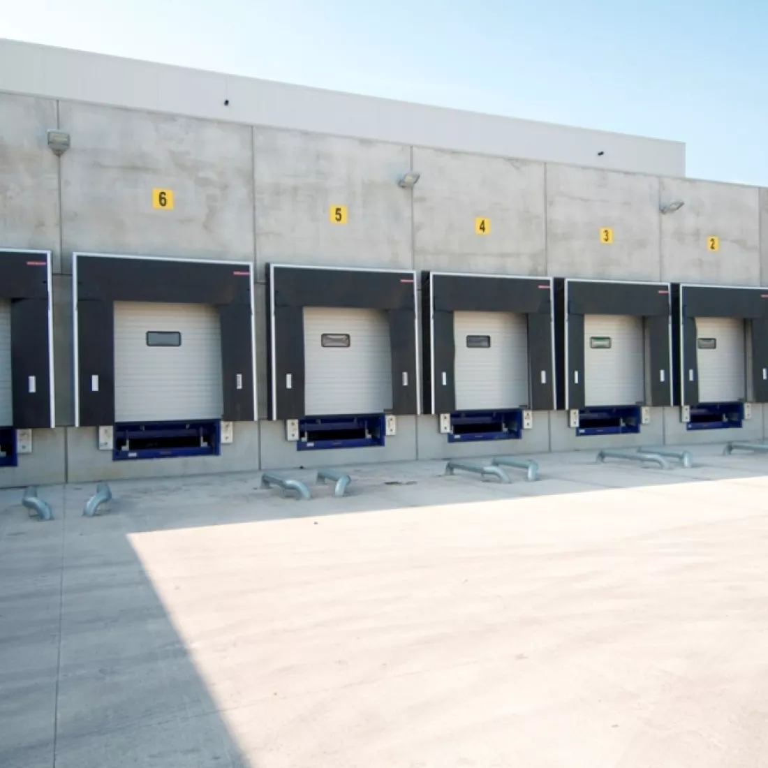 Vooraanzicht dock van koelloodsen Bolckmans. Het gebouw is grijs met witte poorten. Boven de witte poorten hangen gele vierkanten. Op de vierkanten staat een zwart cijfer.
