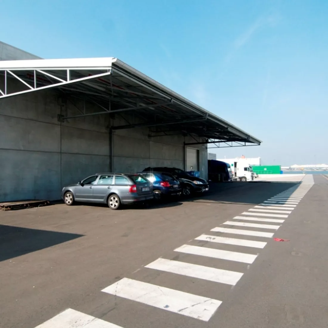 Zijaanzicht magazijn koelloodsen EFP. Links bevindt zich het magazijn met luifel. Onder de luifel staan auto's geparkeerd. Rond het magazijn bevindt zich een zebrapad voor het veilig verplaatsen op het bedrijfsterrein.