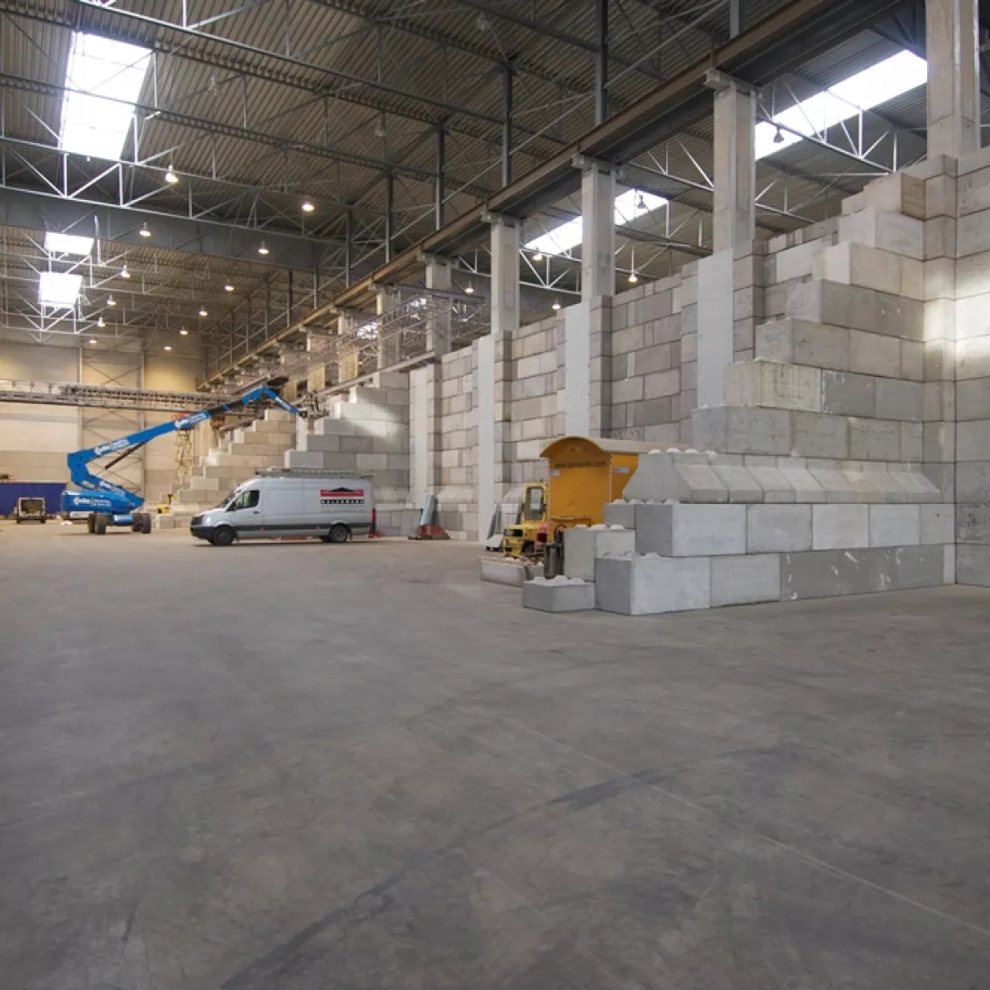 Binnenkant bulkmagazijn Vollers. Er zijn verschillende ruimtes afgebakend met betonblokken. In de verte staat een blauwe hoogwerker en witte camionette.