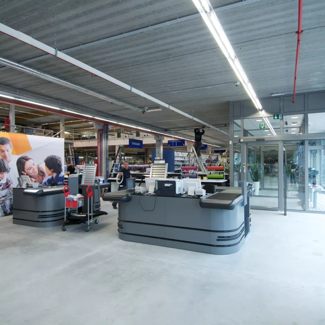 Binnenkant winkel METALeuven. Het is een afbeelding van de kassa's. Er bevinden zicht drie kassa's, deze zijn grijs. Rechts bevindt zich de inkom en links de winkel.