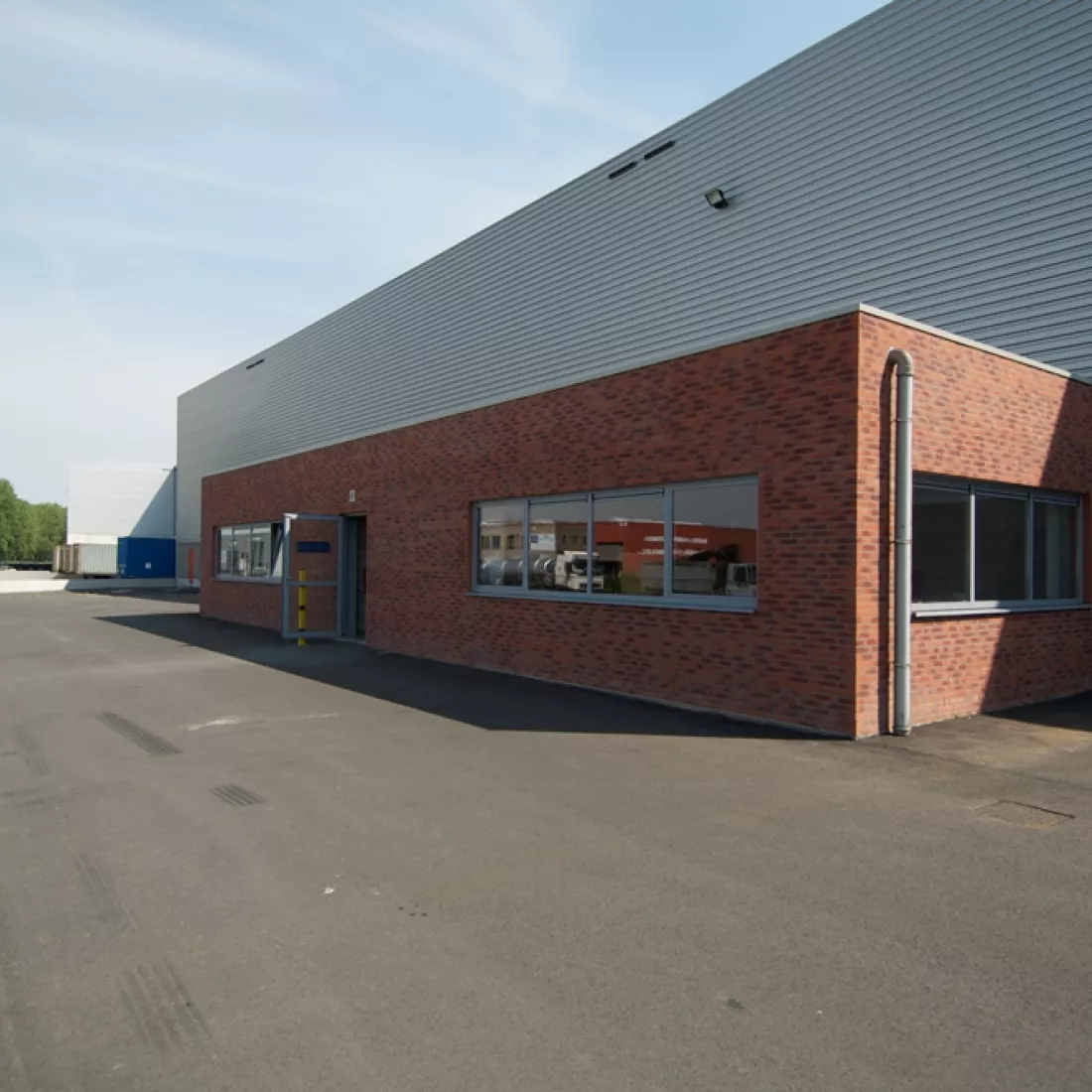 Zijaanzicht distributiecentrum ASL & ASL. Het gebouw tegen het distributiecentrum bestaat uit rode steen en bevat ramen met grijze omranding.