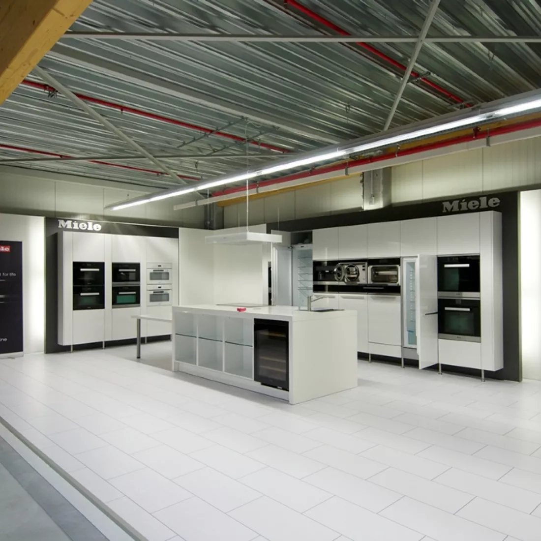 Binnenkant winkel METALeuven. De afbeelding is van een tentoongestelde keuken van Miele. De keuken is wit en bevat een keukeneiland.