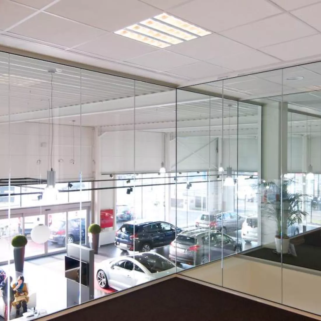 Binnenkant Peugeot garage - Gabriel Car. De afbeelding is genomen vanaf de tweede verdieping. Je kan de gelijkvloers zien door de glazen ramen van de kantoren. Op de gelijkvloers is de showroom.