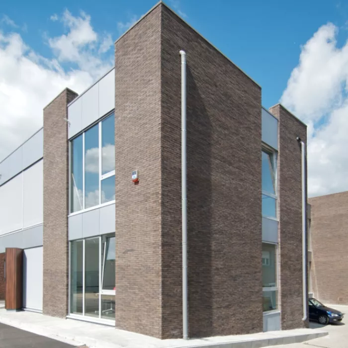 Zijaanzicht Frateur De Pourcq. Het gebouw bestaat uit grijze stenen in combinatie met grijze platen. Het gebouw heeft veel ramen.