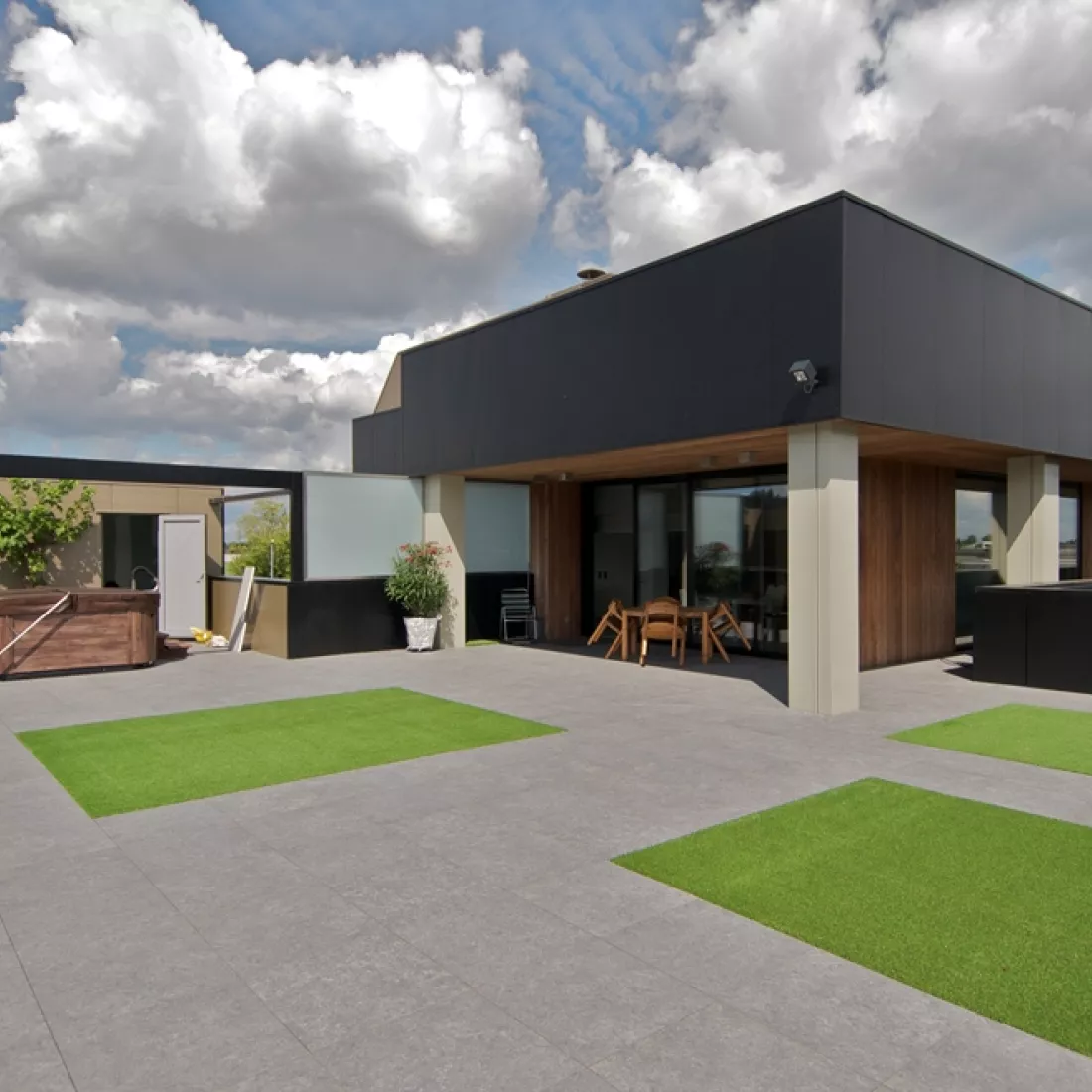Bovenste verdieping bedrijfspand Vitra. De afbeelding is genomen vanop het balkon. Het is een ruim terras dat bestaat uit grijze stenen en enkele stukken gras.