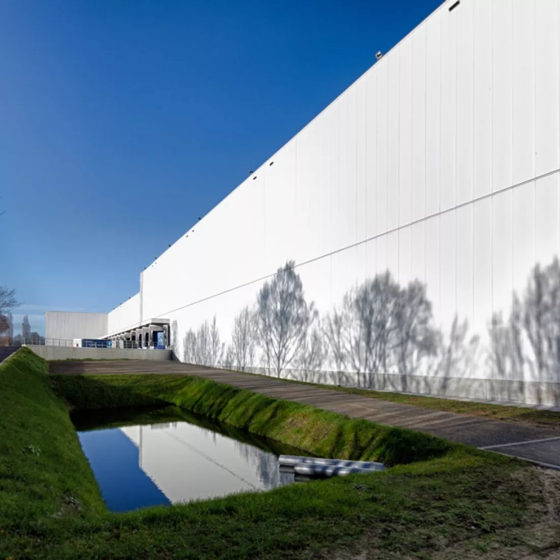 Zijaanzicht dock - Sabert. Het gebouw bestaat uit witte platen en het dock bevat blauwe poorten.