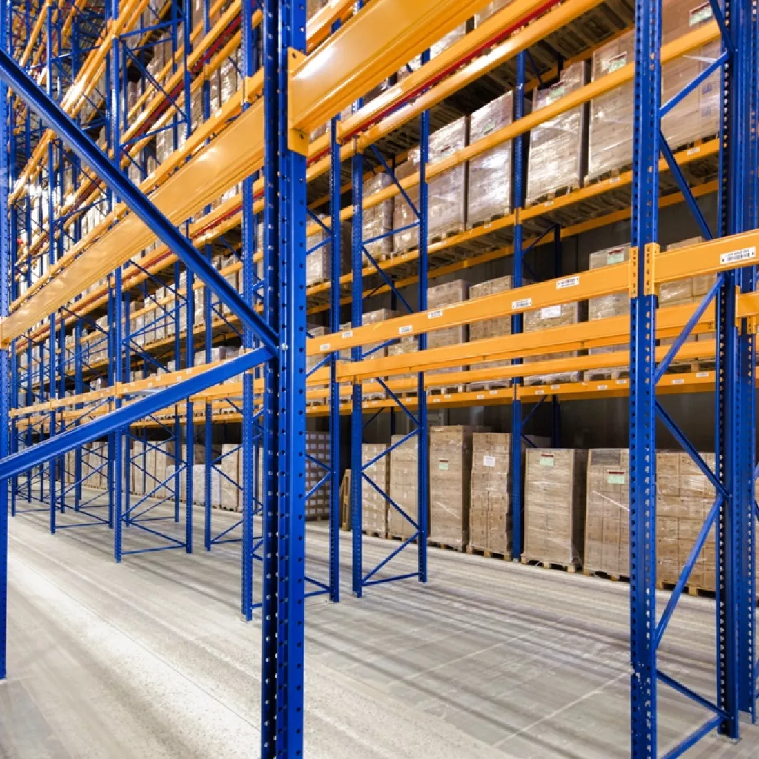 Binnenkant opslagplaats - Sabert. Er bevinden zich blauwe met oranje rekken om materialen op te slagen. Helemaal rechts staan er al materialen in de rekken.