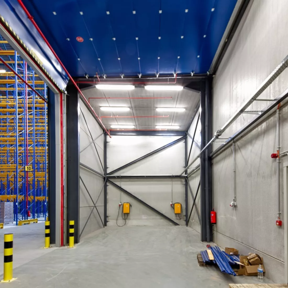 Binnenkant opslagplaats - Sabert. Het gebouw bestaat uit een combinatie van materialen zoals beton. Links bevinden zich de rekken. Een deel van het plafond is blauw.
