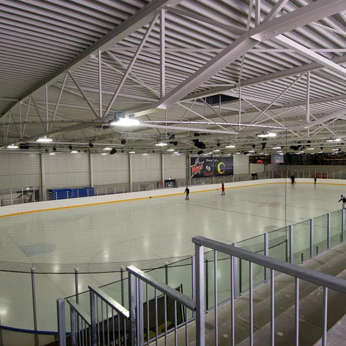 Zijaanzicht binnenkant Ice Skating center. Bij de opbouw van de overdekte ijspiste werd staal gebruikt. In het midden is een grote ovale ijspiste. Rechts hiervan staat een tribune.