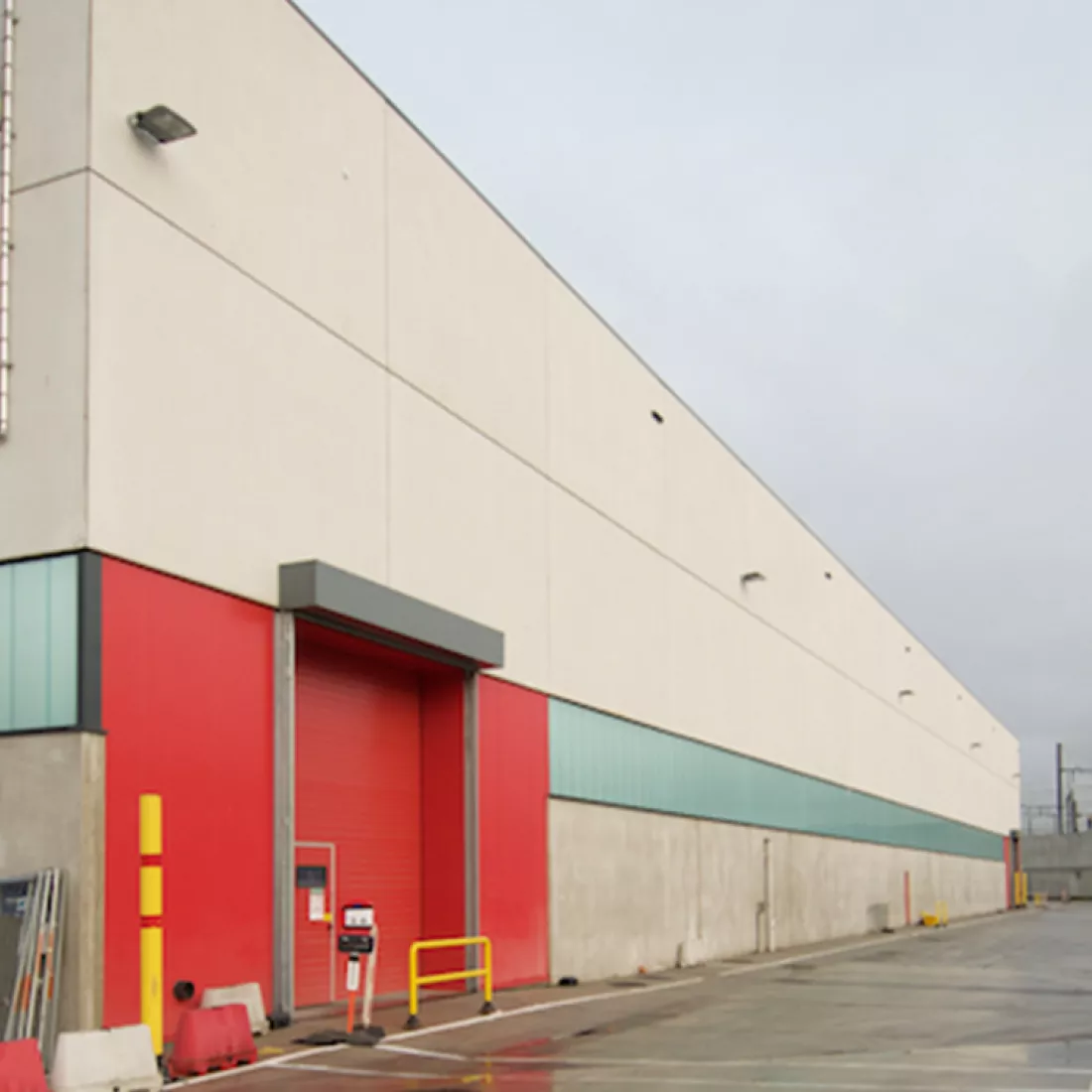 Magazijn AB Inbev. Het gebouw is grijs en heeft een rode poort. Het magazijn bevindt zich links op de afbeelding.