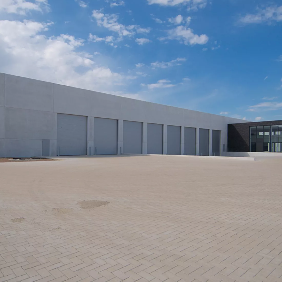 Zijaanzicht productiehal en kantoren Alcom. Links bevindt zich de productiehal met grijze poorten. Rechts van de productiehal de zwarte kantoren.