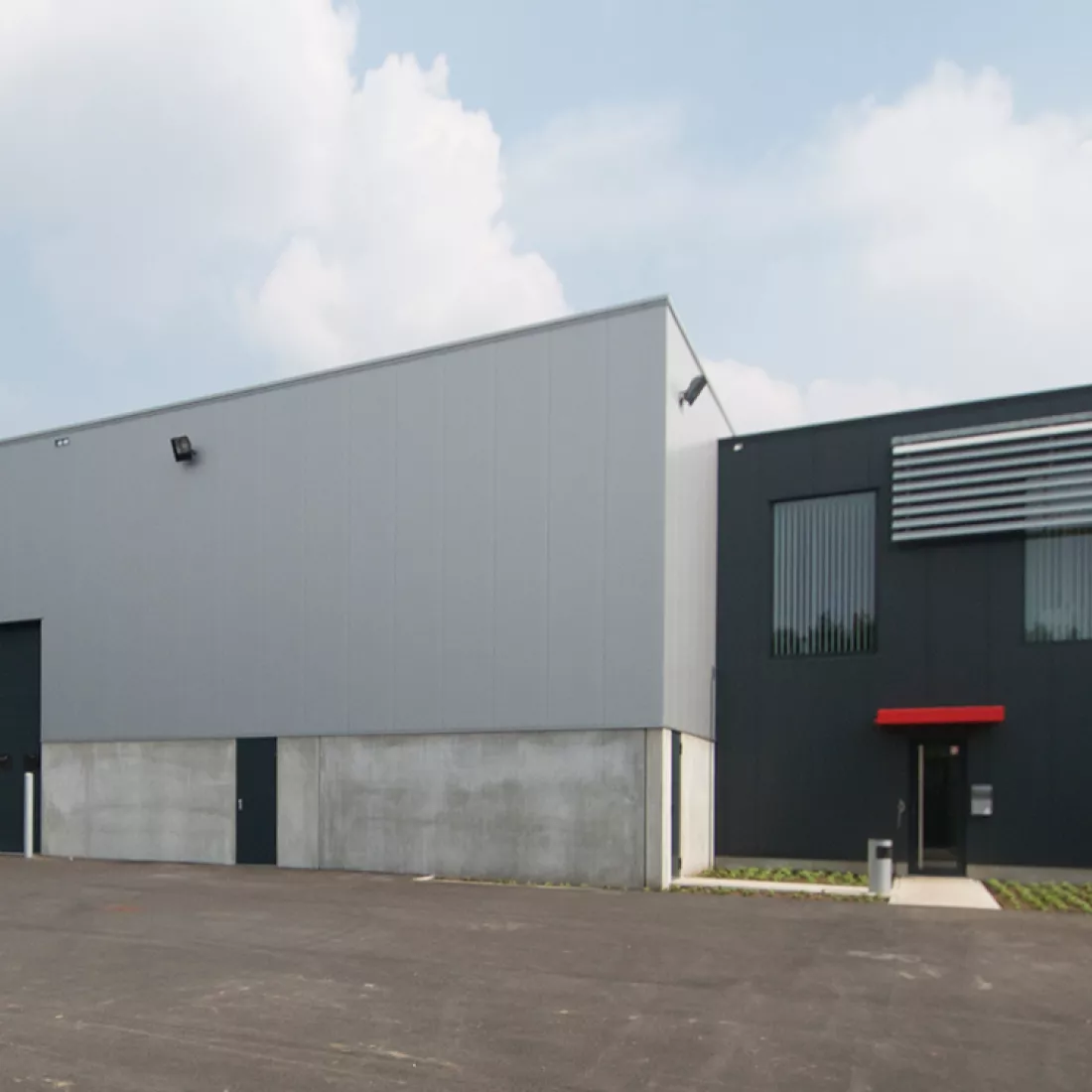 Vooraanzicht werkplaats Hansea voor bussen met kantoren.Bij de bouw van het gebouw is er staal gebruikt. Rechts bevindt zich wat meer naar achter een zwart gedeelte van het gebouw, dit is het kantoor. De linkerkant van het gebouw is grijs met zwarte poorten en deuren, dit is het magazijn.