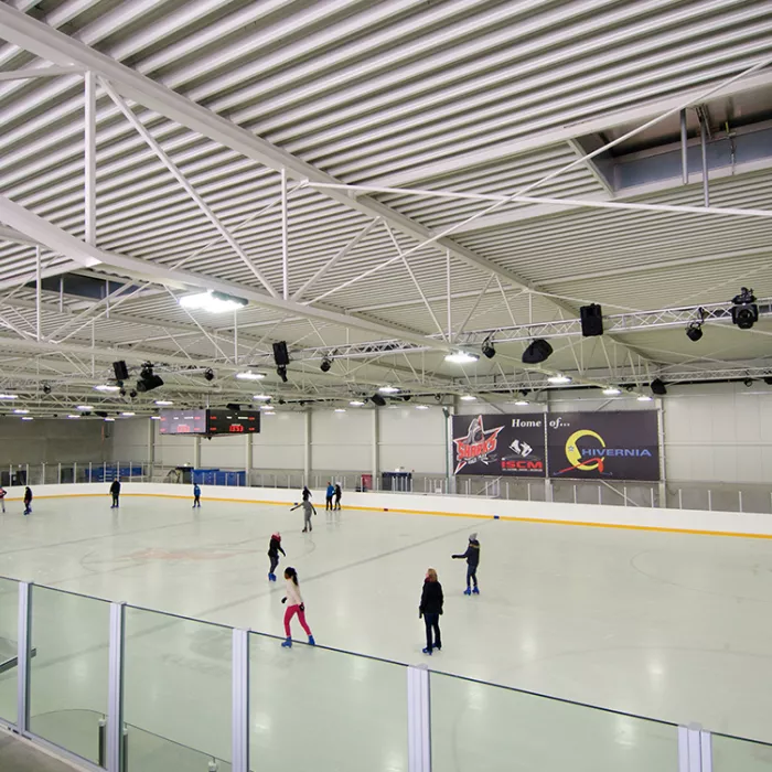 Binnenkant Ice Skating center. Er zijn mensen aan het schaatsen op de ijspiste. Tijdens de opbouw van de hal is staal gebruikt.