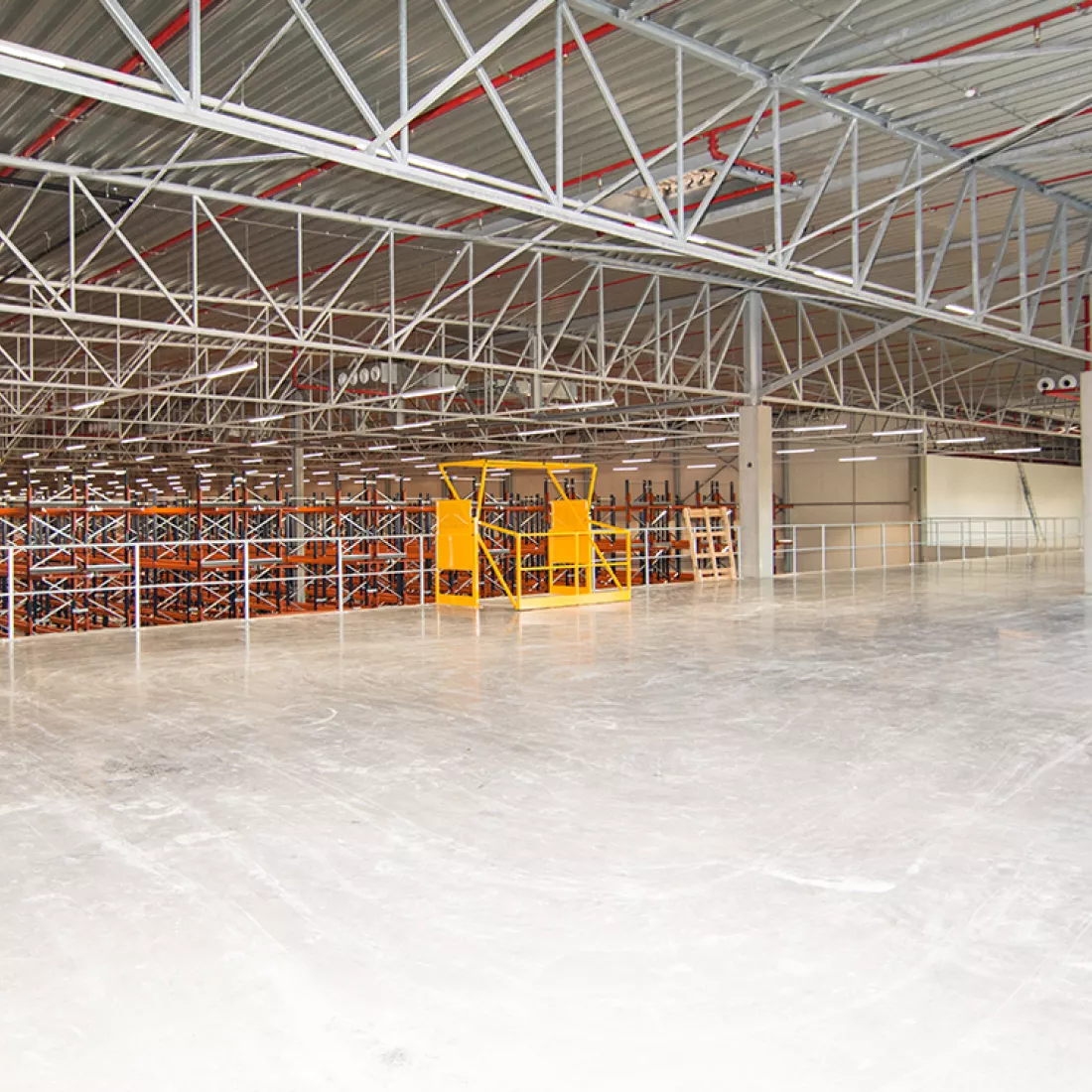 Binnenkant magazijn - Keetberg Logistics Center. De afbeelding is genomen vanaf de tweede verdieping. De verdieping is afgesloten met een railing. Je hebt vanaf deze verdieping dus zicht op de gangen met rekken in het magazijn.