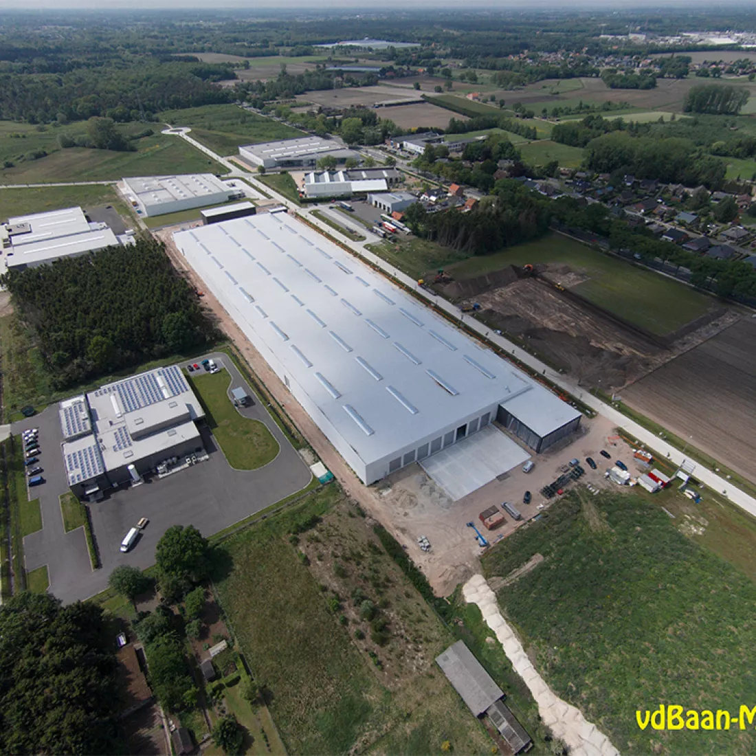 Bovenaanzicht productiehal en kantoren Alcom. De productiehal is een lang, rechthoekig gebouw. Rechts tegen de productiehal bevindt zich het kantoor.