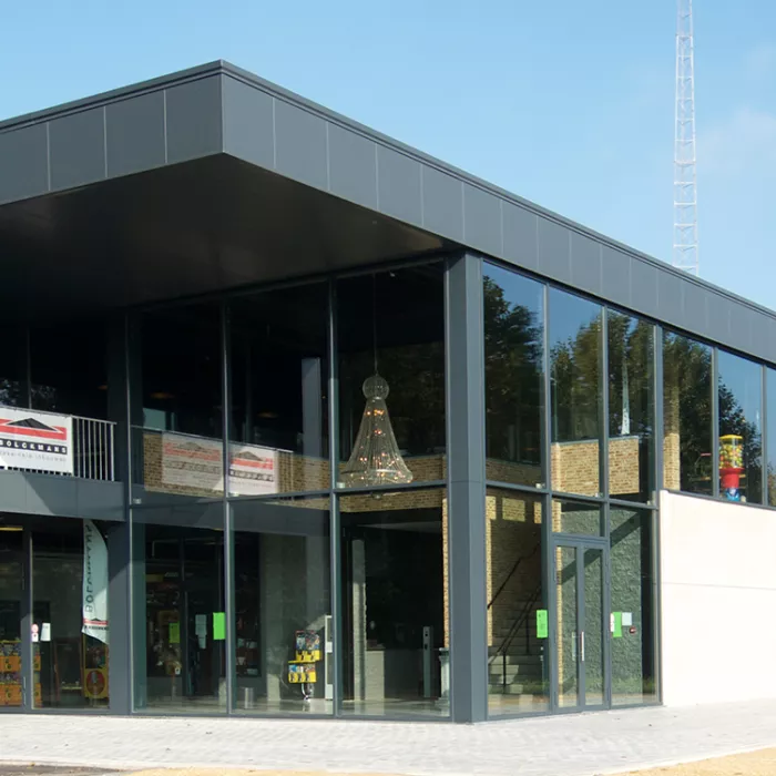 Buitenkant Ice Skating center. Het gebouw heeft grote ramen. Het bestaat uit beton en zwarte platen. Tijdens de opbouw is staal gebruikt.