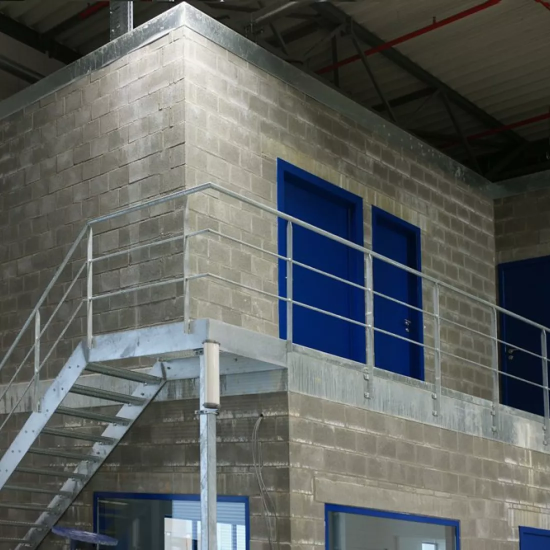 Binnenkant distributiecentrum Miko. In het distributiecentrum staat een gebouw met twee verdiepen. De deuren hier zijn blauw en er loopt een trap naar de eerste verdieping.