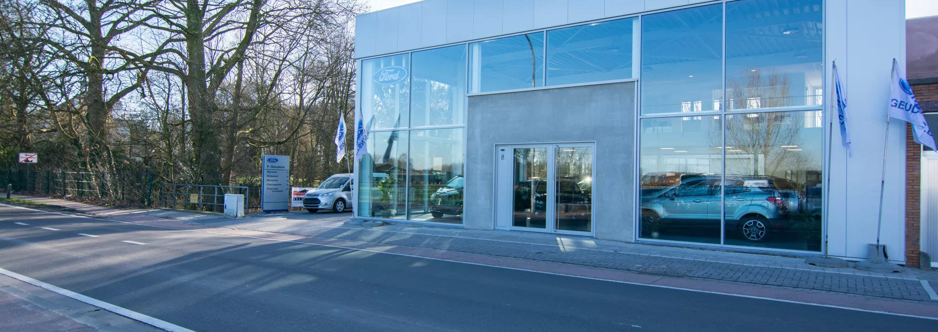 Vooraanzicht showroom Geudens. Het gebouw is grijs en bevat grote ramen. Tijdens de opbouw is staal gebruikt.