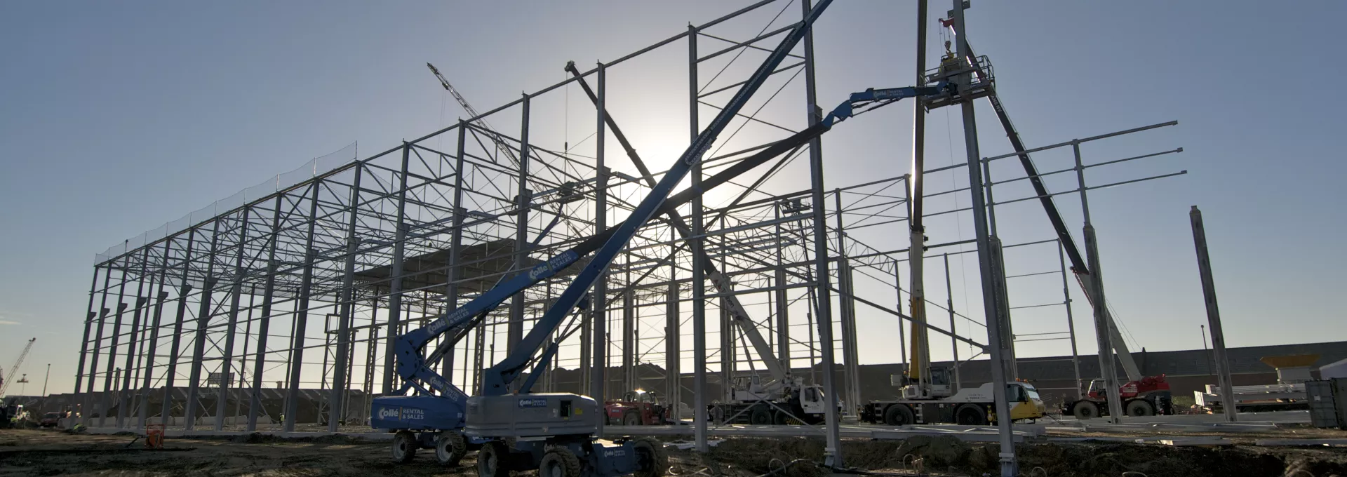 een bouwplaats met een stalen framestructuur die het skelet van het gebouw vormt, met een kraan in de voorgrond.