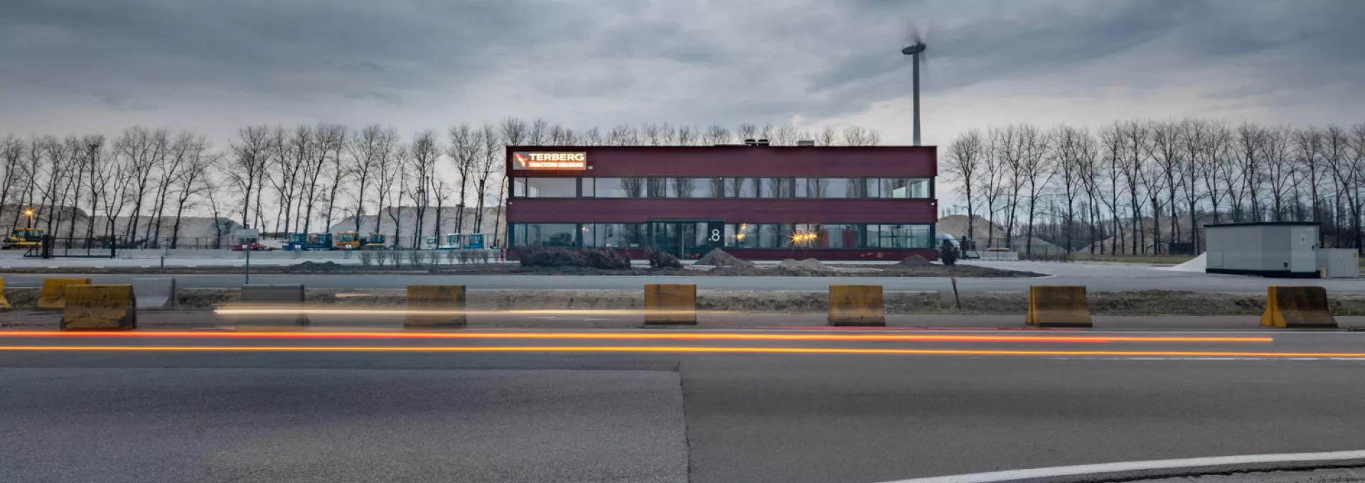 Vooraanzicht bedrijfspand Terberg Gent. Het gebouw is rood en heeft twee verdiepen. Zowel de onderste als bovenste verdieping bestaat uit grote ramen met zwarte omkadering. Bovenaan links hangt het logo van Terberg. Het gebouw is gebouwd uit staal.