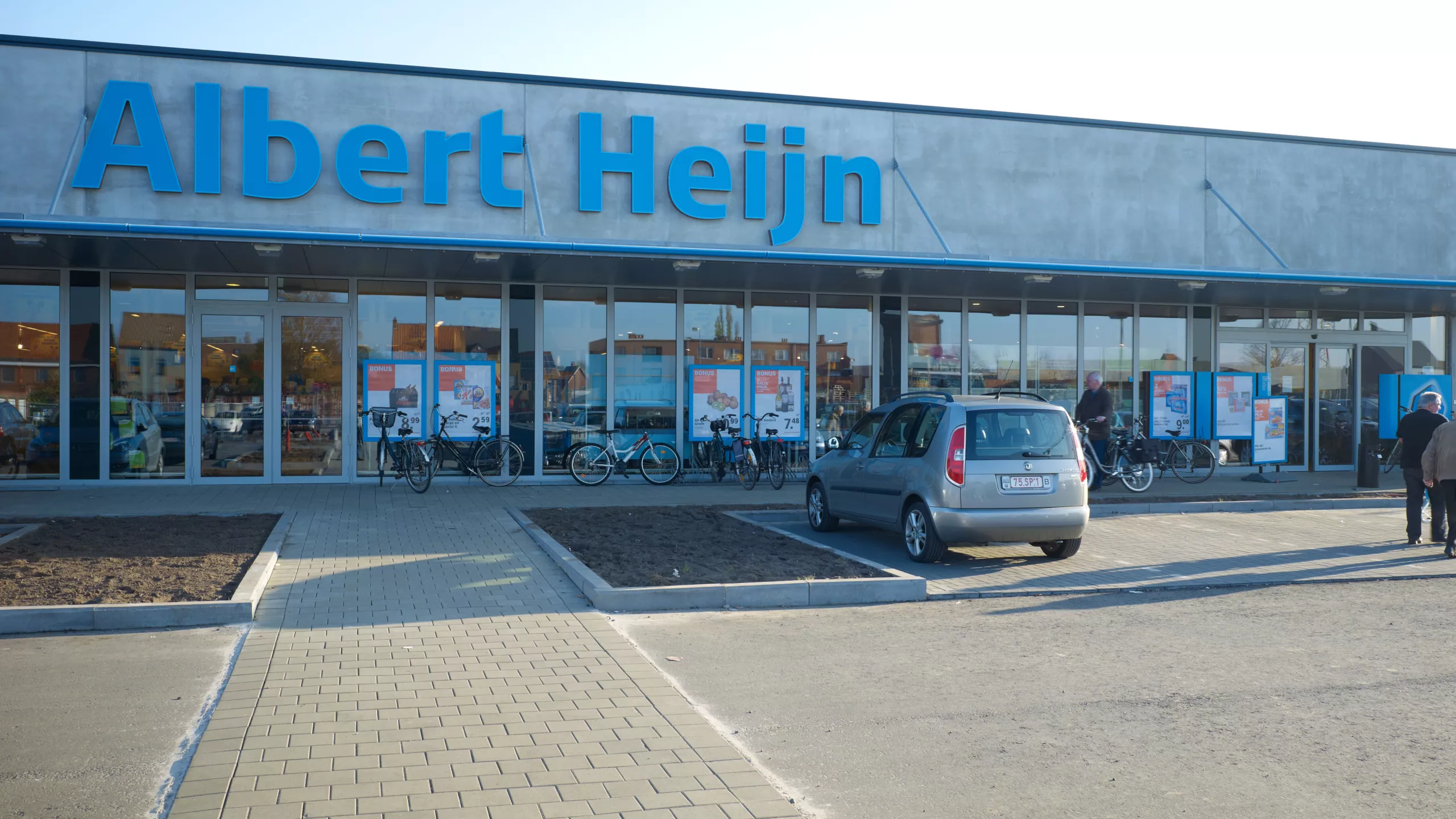 KMO Units Picolo - Van Ende. De afbeelding is een vooraanzicht van de Albert Heijn. Voor de winkel zijn parkeerplaatsen voorzien. Tijdens het bouwen van de units is er een combinatie van materialen gebruikt.