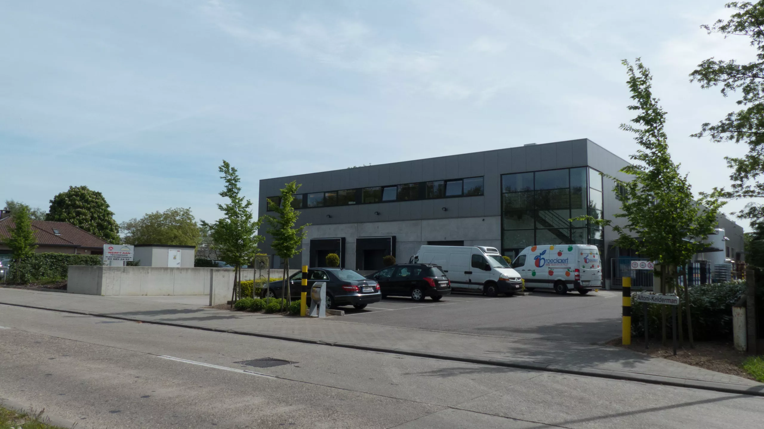 Bouwen en verbouwingen voor Kelkro. De afbeelding is een zijaanzicht van het werkgebouw. Er is een dock aanwezig. Rechts voor het gebouw is er parking voorzien. Het gebouw bestaat uit twee verdiepingen en is opgebouwd met beton.
