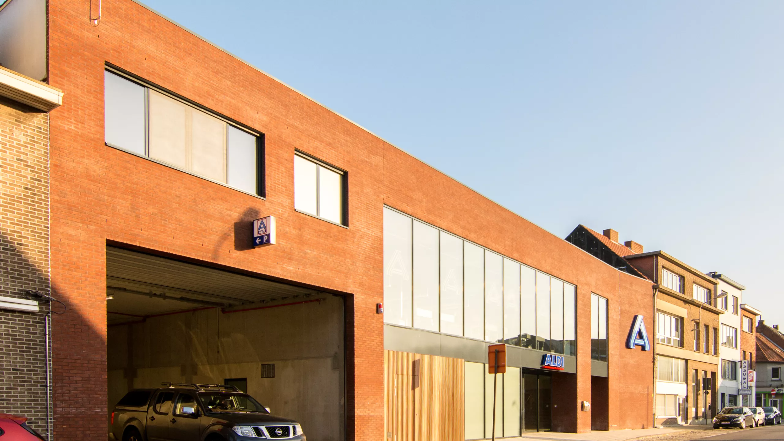 Aldi met overdekte parking. De winkel en parking werden gebouwd met een combinatie van materialen. Het gebouw bestaat uit een rode steen en bevat grote ramen.