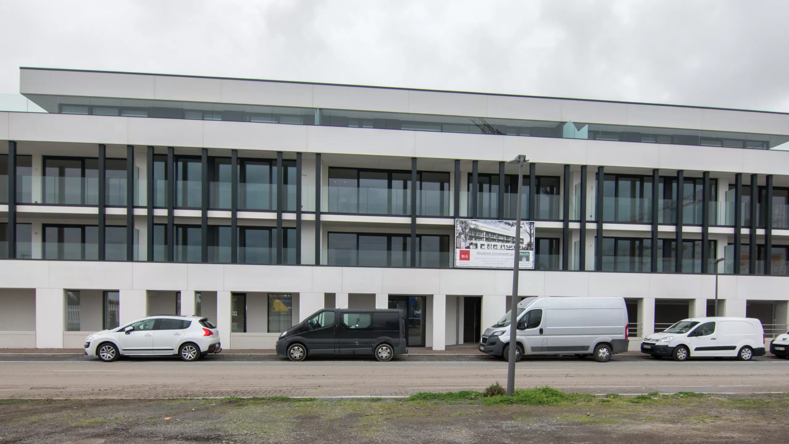 Duin & Water shops. Duin & Water shops. Het gebouw is gebouwd met beton. Het bestaat uit witte platen. Het heeft vier verdiepingen. De bovenste drie verdiepingen hebben een balkon. Bij elk balkon bevinden zich zwarte balken.
