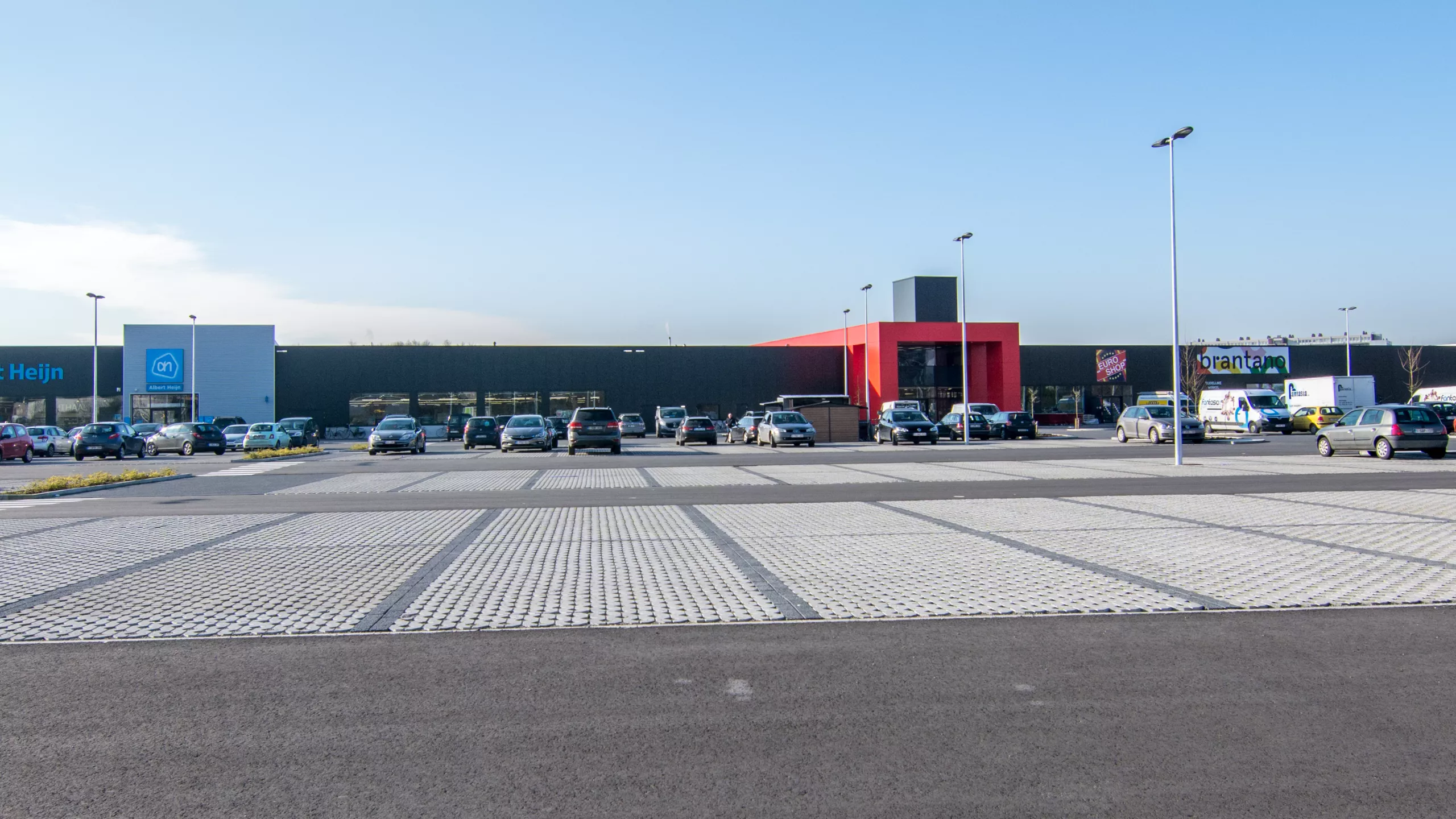 Uitbreiding handelsruimten en parking Immo Euro. De afbeelding is een vooraanzicht van het gebouw. Het gebouw is opgebouwd met beton. Voor het gebouw bevindt zich een grote parking.